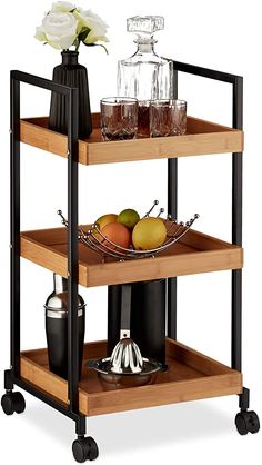 a three tiered serving cart with drinks and fruit on the bottom shelf, in front of a white flower