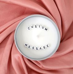 a white candle with the words custom message written on it surrounded by pink satin material