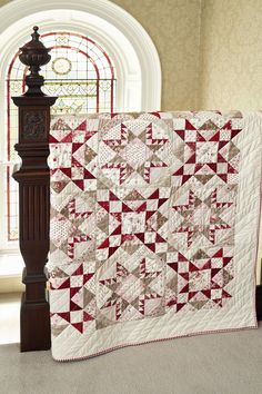 a large red and white quilt sitting on top of a wooden pole next to a window