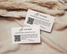 two white business cards sitting on top of a fur covered bed next to each other