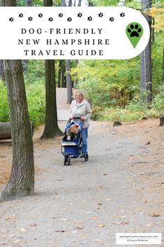 a woman pushing a stroller with a dog in it on a path surrounded by trees