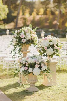 two vases filled with flowers sitting on top of a grass covered field next to white chairs