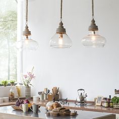 three lights hanging from the ceiling above a kitchen counter with food and drinks on it