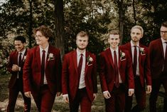 a group of men in red suits and ties standing next to each other near trees