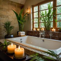 candles are lit in front of a bathtub with plants and towels on the counter