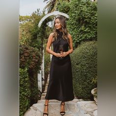 a woman in a black dress is holding a glass of wine and standing on some steps