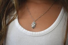 a woman wearing a silver necklace with a leaf charm on it's neck,