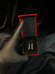 a pair of earrings in a red box on a black cloth covered table with gloves