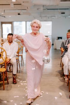 an older woman is walking down the aisle with her hands in her pockets and throwing petals into the air