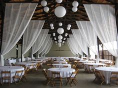 tables and chairs are set up in an open room with white drapes hanging from the ceiling