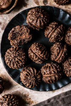 chocolate cookies on a black plate next to some nuts