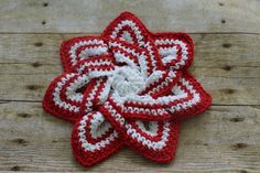 a crocheted red and white flower sitting on top of a wooden table