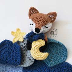 a crocheted stuffed animal sitting on top of a pile of blue and yellow blankets