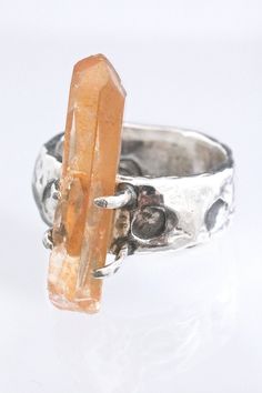 "A natural tangerine quartz crystal is set on a rustic silver ring. Hand fabricated from solid sterling silver with hammered texture and organic shaping to create an ancient feel. Orbs or moons are stamped around the band. The bright orange crystal is held in by four claw like prongs. Oxidized and rubbed back for a dark patina in recesses. One of a kind, created by the artist, Miche McClendon, in her Laguna Beach studio/gallery. A crescent moon is stamped inside the band with a handmade stamp to Moon Stamp, Witch Ring, Ring Magic, Beach Studio, Tangerine Quartz, Witch Rings, Magic Crystal, Gothic Ring, Handmade Stamps