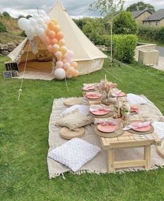 a table set up with plates and balloons in the grass for an outdoor birthday party