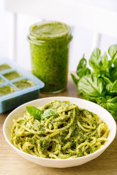 a white bowl filled with pesto pasta next to a container of pesto sauce