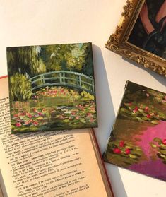 an open book sitting on top of a table next to two pictures and a painting