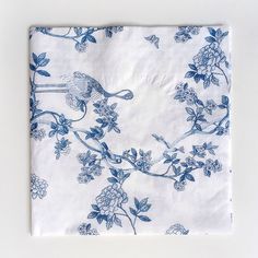 a blue and white floral print napkin on a white tablecloth with an image of a bird perched on a branch