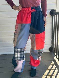 a woman standing on a porch with her hands in her pockets and wearing colorful pants