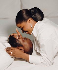 a man and woman laying on top of a bed next to each other with their hands touching foreheads