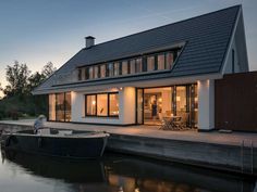 a boat is parked in front of a house on the water's edge at dusk