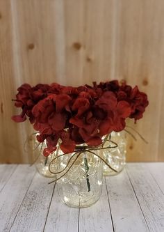 red flowers are in glass vases on a white wooden table with wood planks