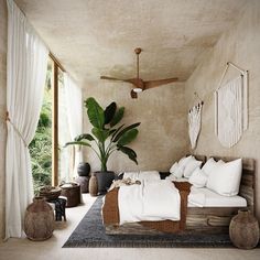 a bed with white sheets and pillows in a room next to a plant on the floor