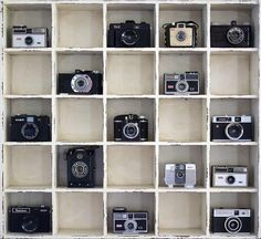 several different types of cameras on display in a wooden shelf with white paint and black trim