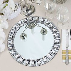 a round mirror sitting on top of a table next to silverware and flowers in vases