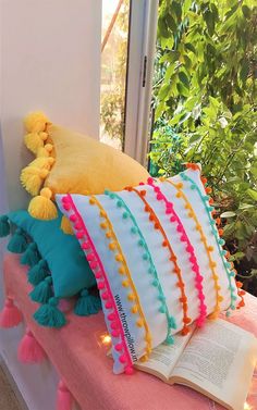 colorful pillows and books on a bench in front of a window