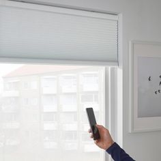 a person holding a remote control in their hand near a window with blinds on it