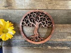 a vase with yellow flowers and a metal tree ornament on a wooden surface