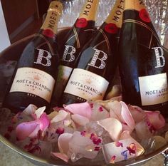 three bottles of wine are sitting in a bowl with pink flowers on the table next to it