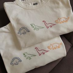 two t - shirts with embroidered dinosaurs on them