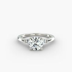 a white gold engagement ring with three stones on the side and a round brilliant diamond center