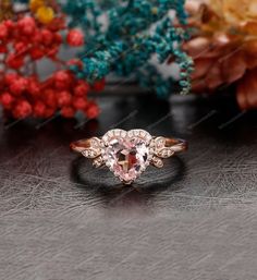 a pink diamond ring sitting on top of a table next to some flowers and red berries