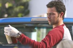 a man in red shirt and white gloves holding a can of paint next to a blue car