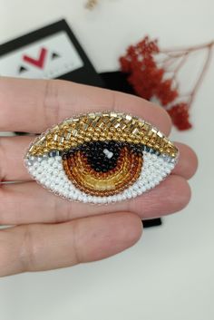 a hand holding a beaded brooch depicting an eye