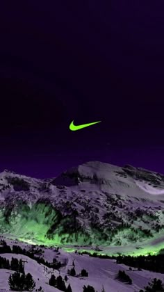 a green and black nike logo is in the sky above snowy mountains at night time