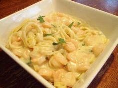 a white bowl filled with pasta covered in shrimp and sauce on top of a wooden table