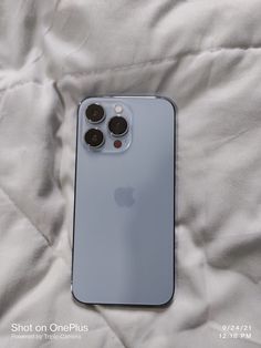 an iphone 11 pro sitting on top of a white bed with the cover pulled down