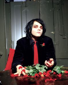 a man in a suit and tie sitting at a table with red roses on it