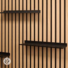 three black shelves are on the wall with wood slats behind them, and one shelf has a flower in it