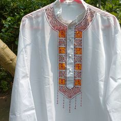 a white shirt with an orange and red design on the front, hanging from a tree