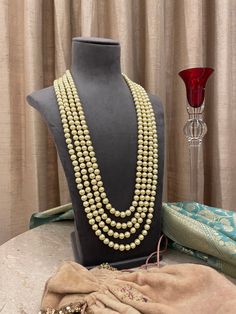 We are proud of our prestigious heritage in this 4 strand pearls groom mala for the bridegroom! A necklace that upholds traditions is royal and elegant. Perfect for the grooms to pair with their sherwanis. Details: Length of Necklace-14.5 Inches All products are manufactured using traditional skills from our rich heritage of crafts.  The process of these crafts is essentially manual. Hence, any irregularities or variations are an inherent part of these handcrafting processes. Festive Kundan Pearl Necklace For Reception, Wedding Temple Necklace With Polished Round Beads, Pearl Bridal Necklace For Reception And Festivals, Pearl Chain Necklace For Reception, Silver Beads For Wedding And Festive Occasions, Festive Gold Beads For Wedding, Traditional Pearl Bridal Necklace For Reception, Silver Wedding Beads For Festive Occasions, Pearl Necklace For Reception