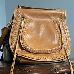 Tan Leather Saddle Style Shoulder Bag In Excellent Used Condition . Adjustable Shoulder Strap And Top Handle With Leather Stitching Detail. Any Markings Are The Natural Leather. Dimensions: Height 10" Width 9-1/4" At Top And 11" At Base Depth: 3-1/4” Brown Saddle Shoulder Bag With Gold-tone Hardware, Cognac Shoulder Bag With Gold-tone Hardware For Errands, Cognac Shoulder Bag With Gold-tone Hardware, Saddle Bag With Gold-tone Hardware For Everyday Use, Brown Crossbody Saddle Bag For Errands, Saddle Bags With Gold-tone Hardware For Everyday Use, Rectangular Leather Flap Bag For Errands, Tan Flap Bag With Removable Pouch For Everyday Use, Everyday Tan Flap Bag With Removable Pouch