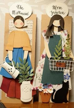 two paper dolls sitting next to each other on top of a wooden table with flowers