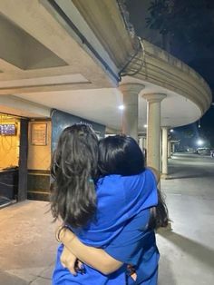 two people hugging each other in front of a building