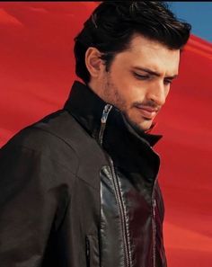 a man wearing a black leather jacket standing in front of a red background