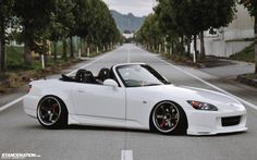 a white sports car parked on the side of a road with trees in the background